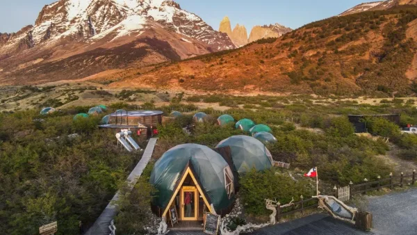 Geodesic dome glamping resort with boardwalks nestled among shrubs below Torres del Paine towers and snowy peaks, Patagonia